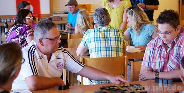 Mehrere Menschen sitzen am Tischen und spielen Qwirkle