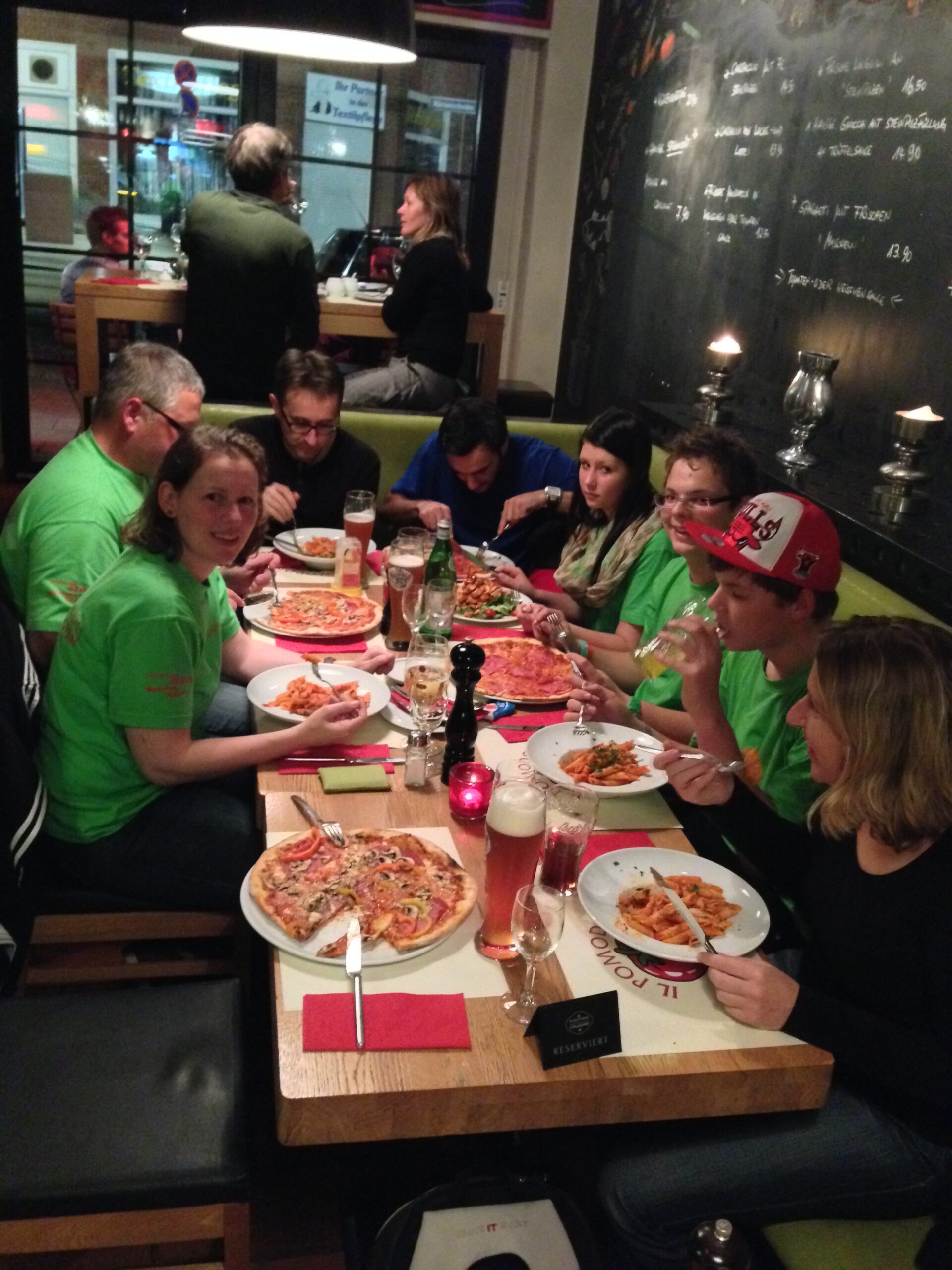 8 Menschen sitzen an einem großen Tisch und jeder hat eine Pizza vor sich stehen und isst sie