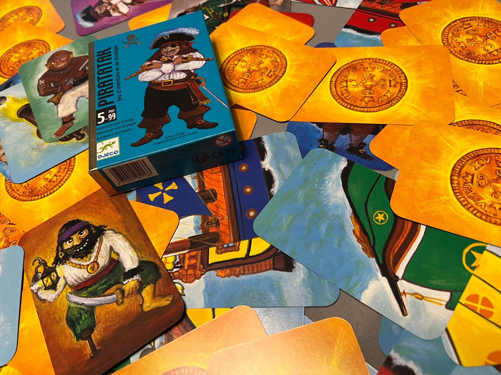 Kartenspiel mit Piratenkarten und vielen Goldmünzenkarten. Die Karten liegen offen und durcheinander auf einen breiten Haufen zusammengeschoben auf dem Tisch